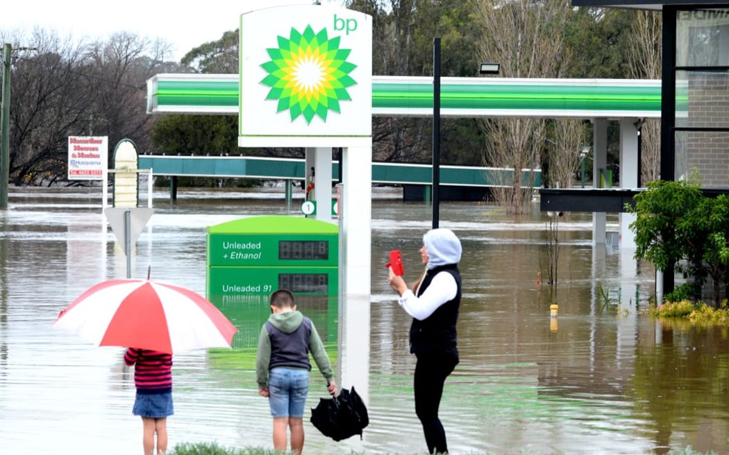 People stand next to a flooded petrol station due to torrential rain in the Camden suburb of Sydney on July 3, 2022. - Thousands of Australians were ordered to evacuate their homes in Sydney on July 3 as torrential rain battered the country's largest city and floodwaters inundated its outskirts. (Photo by Muhammad FAROOQ / AFP)