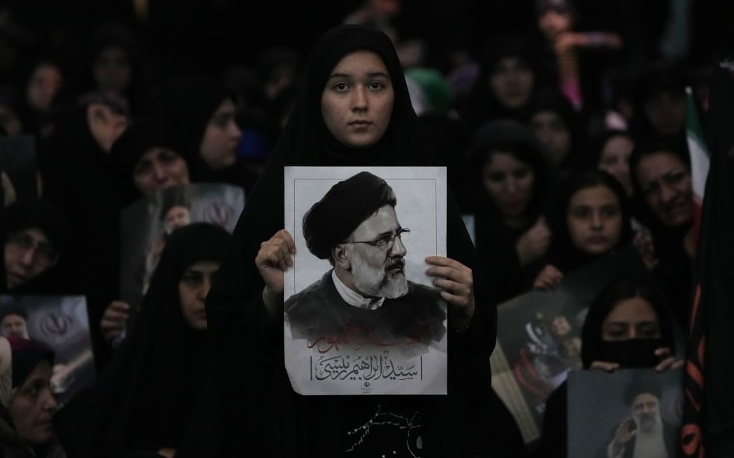 A woman holds a poster of the late Iranian President Ebrahim Raisi  at mam Khomeini Grand Mosque in Tehran, Iran, Tuesday, May 21, 2024, during a funeral ceremony for him and his companions who were killed in a helicopter crash on Sunday in a mountainous region of the country's northwest. Mourners in black began gathering Tuesday for days of funerals and processions for Iran's late president, foreign minister and others killed in a helicopter crash, a government-led series of ceremonies aimed at both honoring the dead and projecting strength in an unsettled Middle East. (AP Photo/Vahid Salemi)