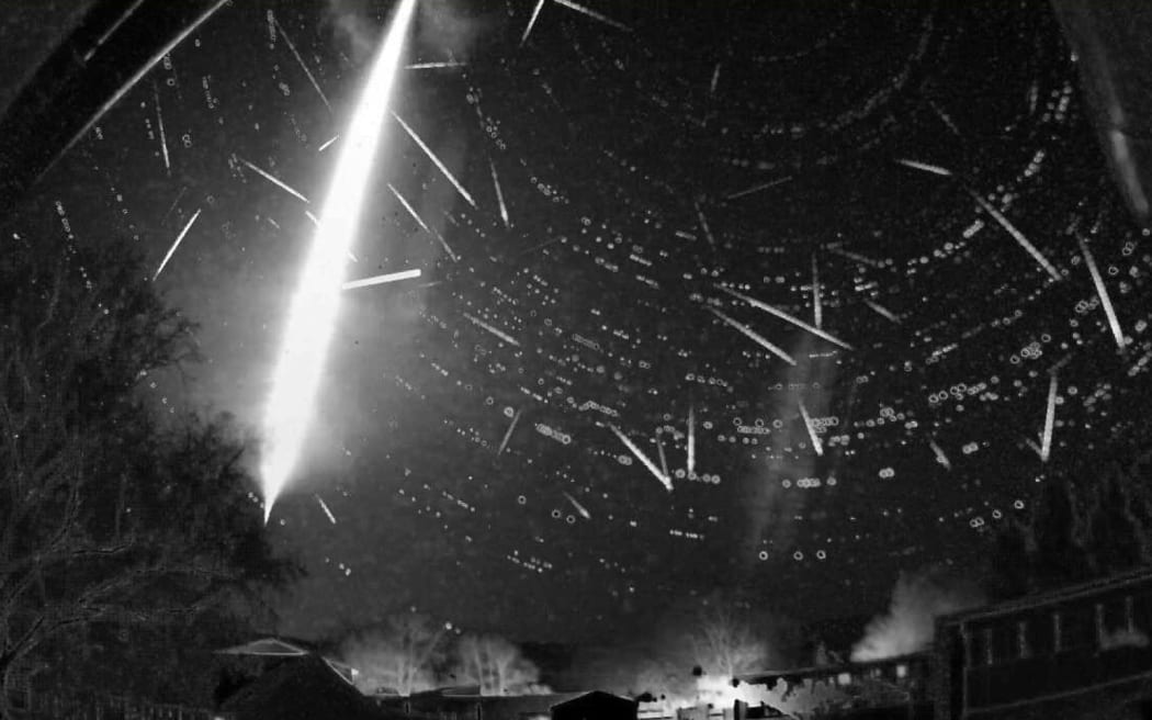 A black-and-white wide-field image of the night sky showing a bright white streak from top to bottom of image. Smaller streaks are visible too.