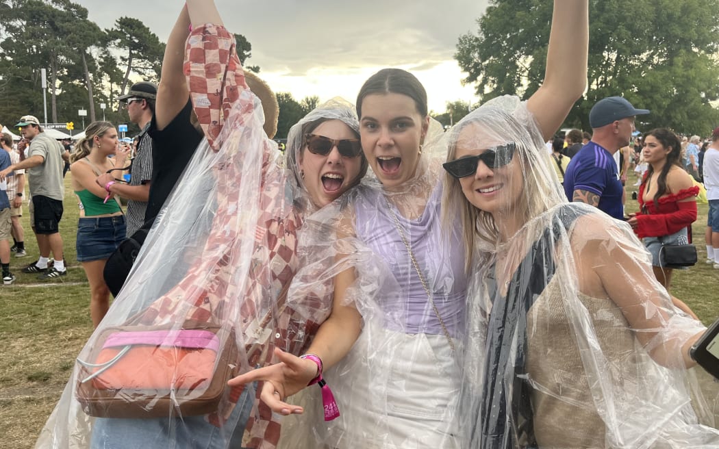 From left: Millie Heime, Megan Blackley and Chloe McMillan continue the festival as the showers hit Electric Avenue yesterday. PHOTO: RNZ / Adam Burns