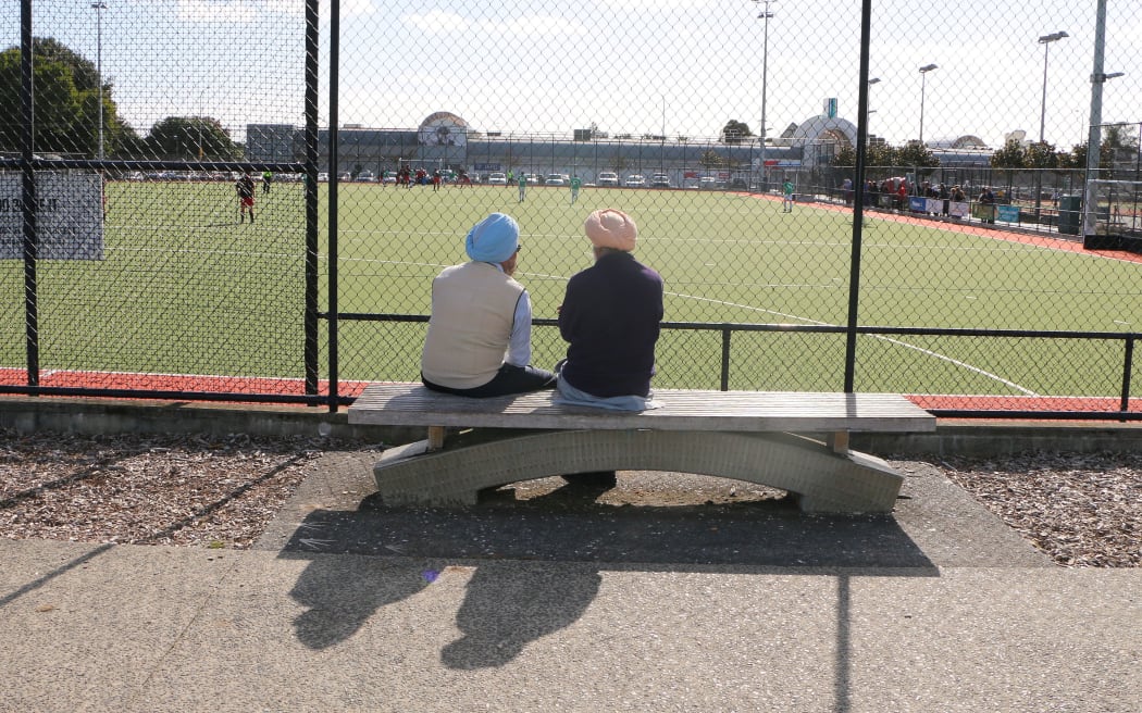 Two Sikh men sit beside a hockey pitch