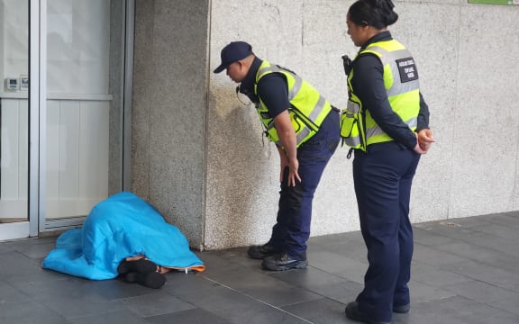 Auckland Council patrollers try to wake up a rough sleeper.