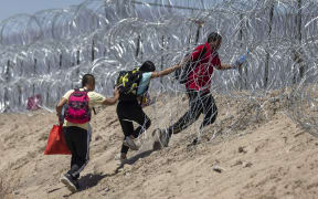 EL PASO, TEXAS - MAY 11: Immigrants walk through razor wire surrounding a makeshift migrant camp after crossing the border from Mexico on May 11, 2023 in El Paso, Texas. The number of immigrants reaching the border has surged with the end of the U.S. government's Covid-era Title 42 policy, which for the past three years has allowed for the quick expulsion of irregular migrants entering the country.   John Moore/Getty Images/AFP (Photo by JOHN MOORE / GETTY IMAGES NORTH AMERICA / Getty Images via AFP)