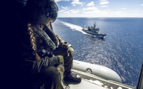 Leading Helicopter Loadmaster Steph Roberts watches HMNZS Wellington as the 6SQN SH-2G(II) Seasprite Helicopter flies nearby.