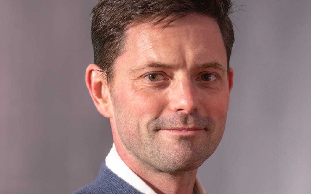 Image of Mike Wesley-Smith smiling at the camera in front of a grey background.