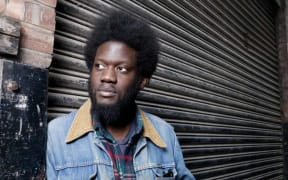 Michael Kiwanuka in a denim jacket leaning against a garage door