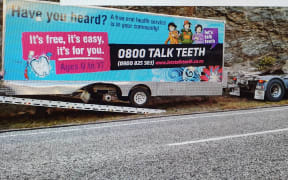 The mobile dental clinic, minus a wheel, is loaded on to the back of a truck near Cromwell.