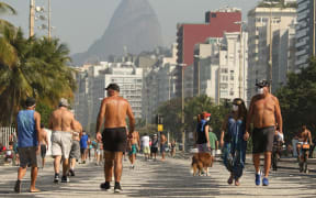 People walk along the edge of Copacabana beach in Rio de Janeiro, Brazil. The country's Covid-19 death toll has surpassed Italy.