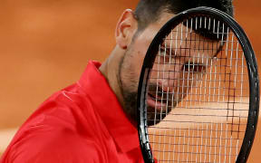 Serbia's Novak Djokovic looks on through his racket during his men's singles semi-final match against Italy's Jannik Sinner on day 13 of the French Open tennis tournament on Court Philippe-Chatrier at the Roland-Garros Complex in Paris on June 6, 2025. (Photo by Alain JOCARD / AFP)