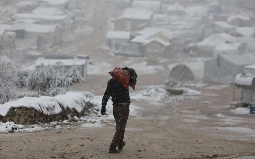 A man carries a sac of charcoal for heating following a snow storm at a camp for some 700 internally displaced Syrians from southern Idlib in Syria's Afrin region in the rebel-held northern Aleppo province on 5 February, 2023.