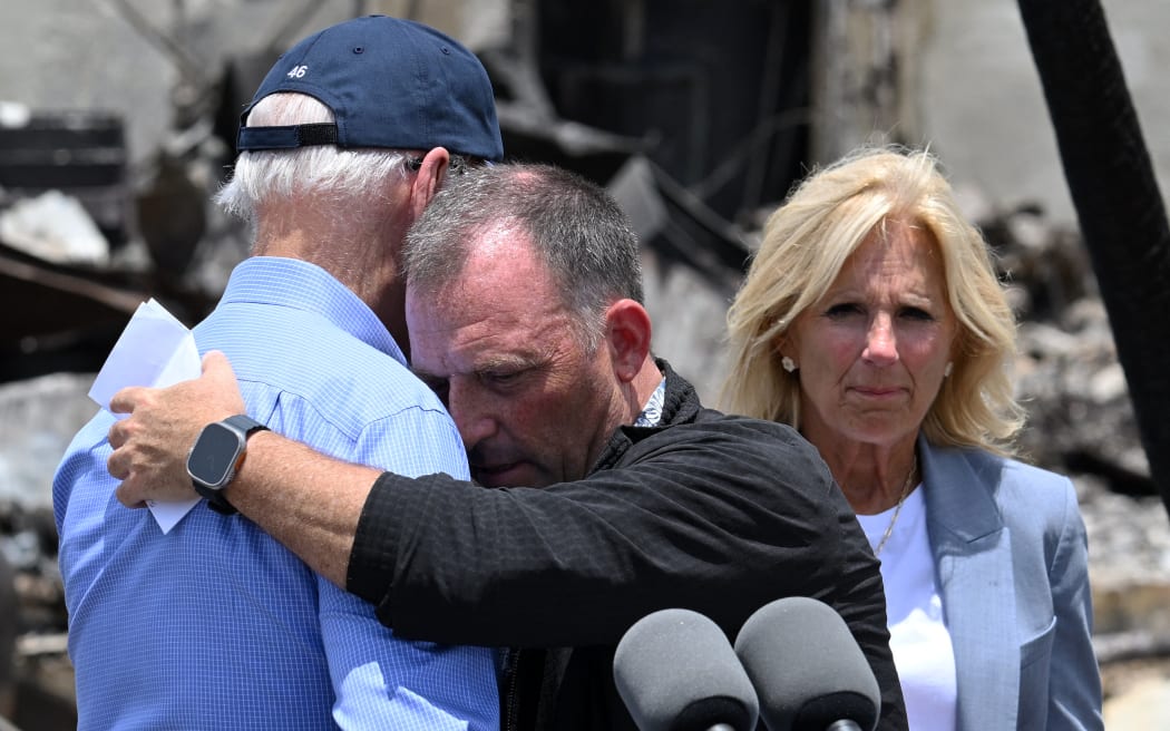 US President Joe Biden is embraced by Hawaii Governor Josh Green (C) after delivering remarks as he visits an area devastated by wildfires in Lahaina, Hawaii on August 21, 2023. The Bidens are expected to meet with first responders, survivors, and local officials following deadly wildfires in Maui. (Photo by Mandel NGAN / AFP)
