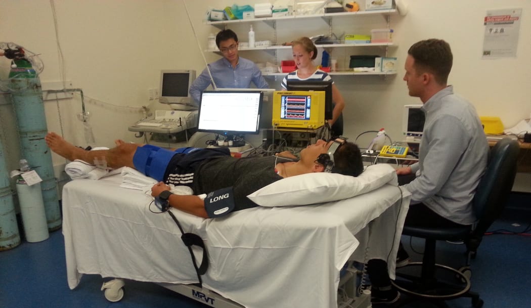 A photo of researchers Shieak Tzeng, Chloe Taylor, Trevor Witter and healthy volunteer AJ on the bed in the clinic