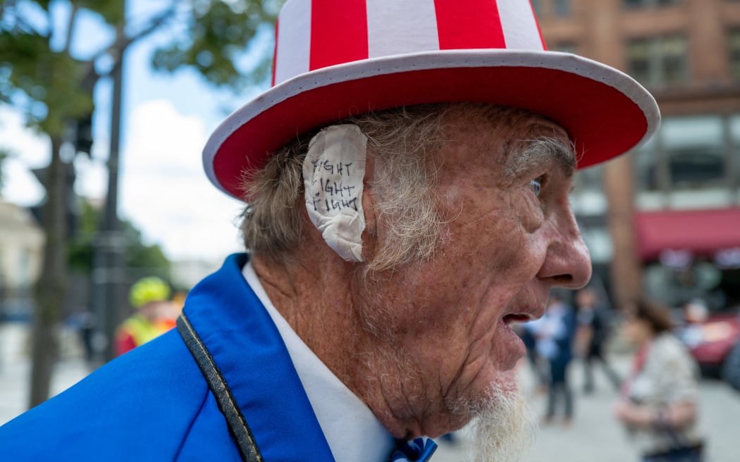 MILWAUKEE, WISCONSIN - JULY 17: A Donald Trump supporter and performer places a bandage over his ear in reference to Trump's wound at the Republican National Convention (RNC) on the third day of the convention on July 17, 2024 in Milwaukee, Wisconsin. Security throughout downtown Milwaukee remains high following the assassination attempt on former President Donald Trump over the weekend. Thousands of delegates, politicians and the Republican faithful are arriving into the traditionally Democratic city over the next few days for the annual convention which will conclude with former President Donald Trump accepting his party's presidential nomination. The RNC takes place from July 15-18.   Spencer Platt/Getty Images/AFP (Photo by SPENCER PLATT / GETTY IMAGES NORTH AMERICA / Getty Images via AFP)