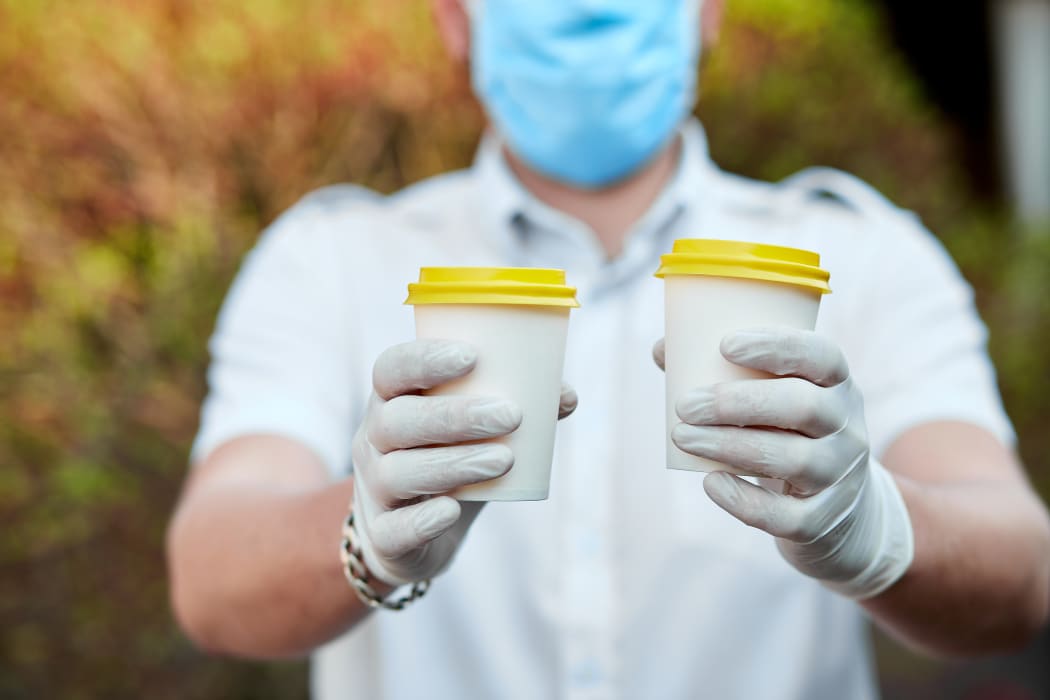 Delivery man in protective mask and gloves, employee hold takeaway cup of coffee. Service quarantine pandemic coronavirus virus Covid-19.