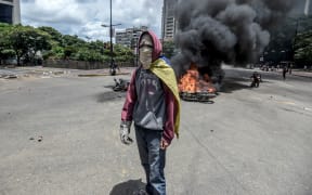 An anti-government activist stands in front of burning police bikes during a protest in Caraca against the elections for a Constituent Assembly.