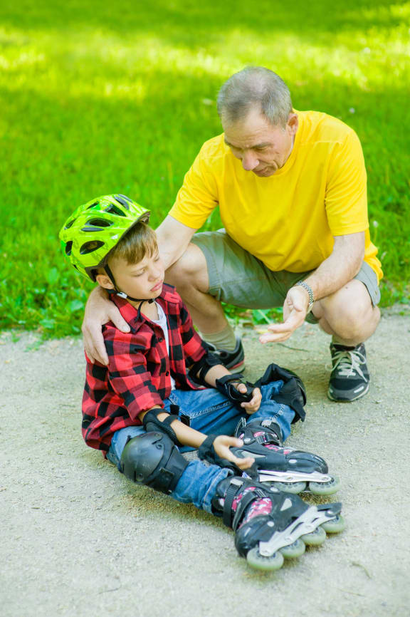 A photo of a father comforting his son who has fallen at skating on the roller skates.