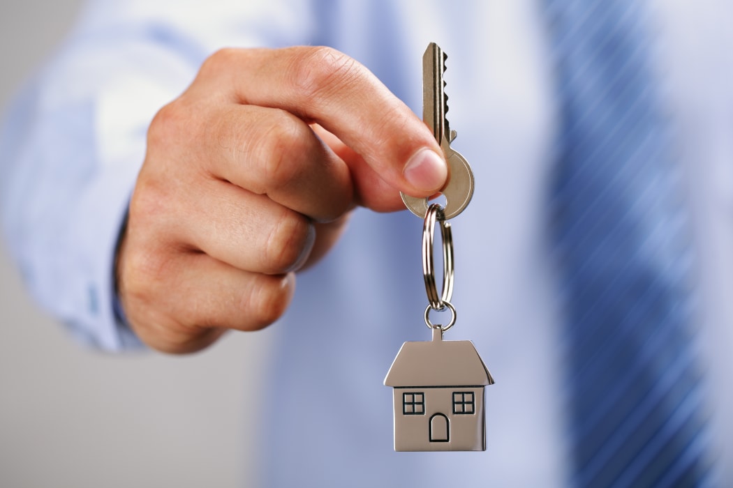A man in a business shirt holds out a set of house keys.