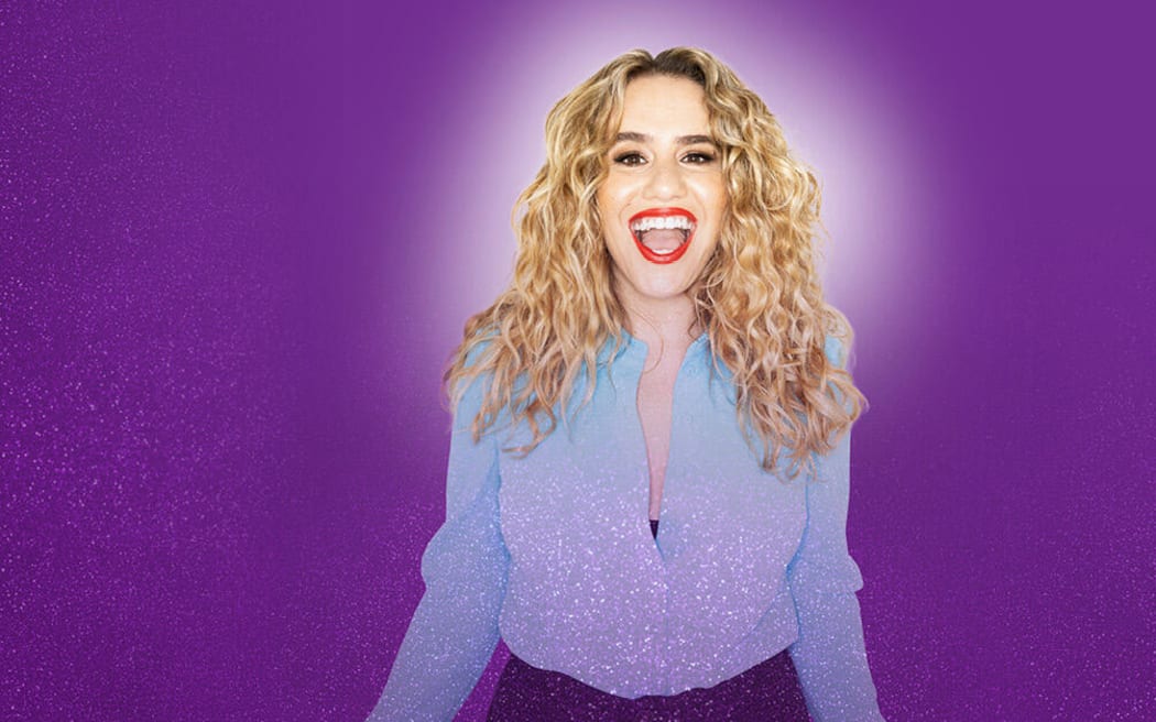 The promotional poster for Michelle Brasier's show REFORM. She stands in front of a purple background smiling.