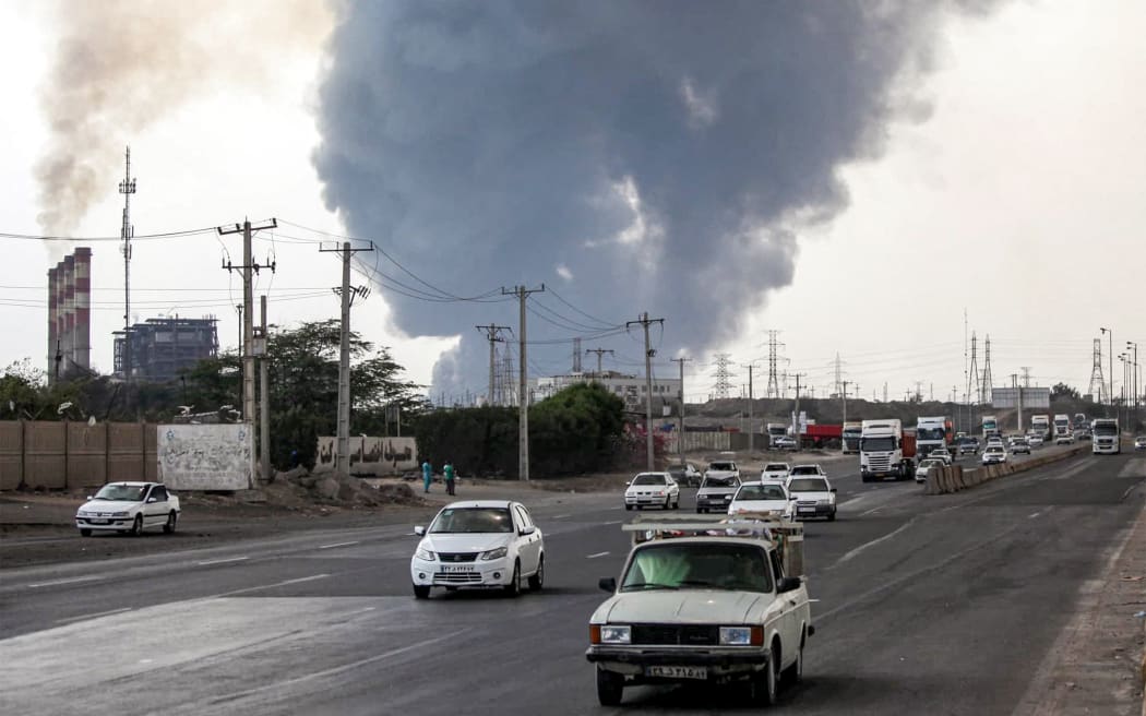 A thick plume of smoke billows as motorists drive their vehicles along a highway near the source of an explosion at the Shahid Rajaee port dock southwest of Bandar Abbas in the Iranian province of Hormozgan on April 26, 2025. Several containers exploded on April 26 at Iran's largest commercial port, authorities said, causing a major blast and fire, and leaving hundreds injured. Shahid Rajaee, more than 1,000 kilometres (620 miles) south of the capital, is the most advanced container port in Iran, according to the official IRNA news agency. (Photo by Mohammad Rasole MORADI / IRNA / AFP)