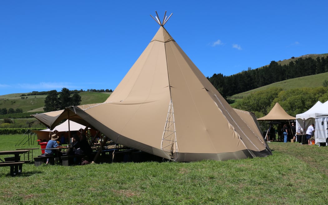 A large teepee-style tent in the middle of a green paddock and against a blue sky.