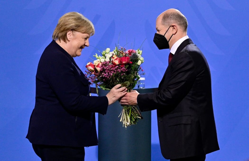 German Chancellor Olaf Scholz gives a bouquet of flowers to his predecessor Angela Merkel after she handed him over the office at the Chancellery in Berlin