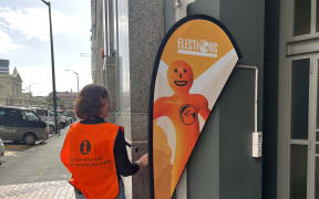 An Electoral Commission worker adjusts a voting sign at a polling station in Stout Street, central Wellington