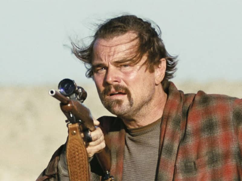 Leonardo DiCaprio holds a gun, his hair is blown around and his face looks wild.