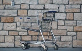 Empty supermarket shopping cart, pointed to left, in front of a stone wall.