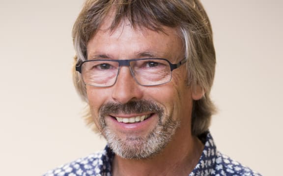 A headshot of a smiling man with sandy brown hair, facial hair and glasses.