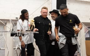 L.A.B. are exiting a small stage carrying golden awards.