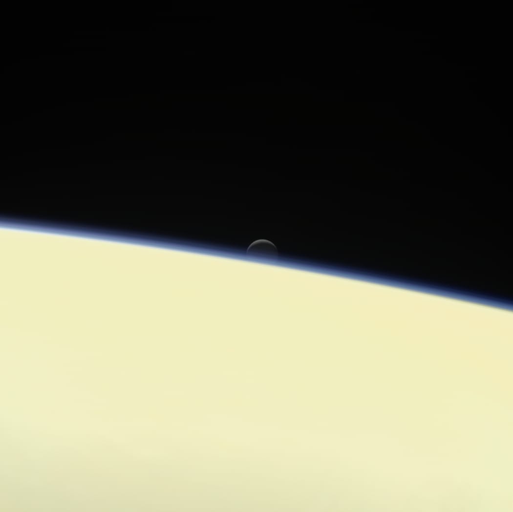 Saturn's active, ocean-bearing moon Enceladus sinks behind the giant planet in a farewell portrait from NASA's Cassini spacecraft.
