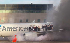This image shows passengers standing on the wing of an American Airlines plane as they are evacuated after it caught fire while at a gate at Denver International Airport in Denver, Colorado, March 13, 2025.