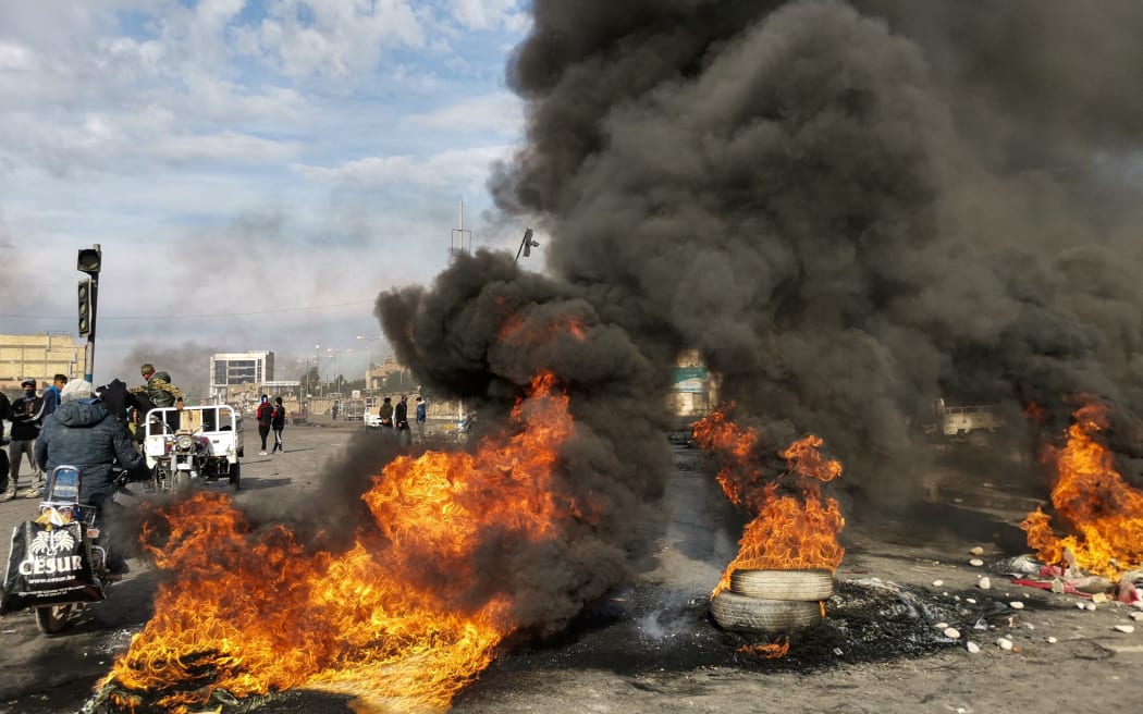Protesters stand by burning tyres at a make-shift roadblock in the city of Nasiriyah in Iraq's southern Dhi Qar province on January 25, 2020