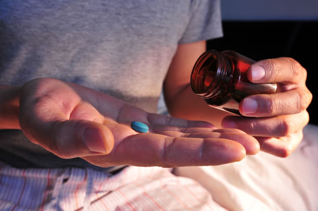 A young man in pajamas in bed about to take a blue pill.