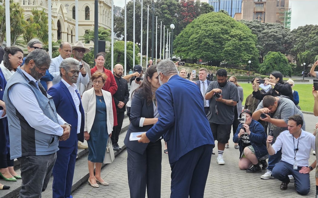 Mātauranga Iwi Leaders Group Chair Rāhui Papa presents a 24,000 strong petition calling for the immediate reversal of the amendment that removed school boards' requirement to give effect to te Tiriti to Minister of Education Erica Stanford.