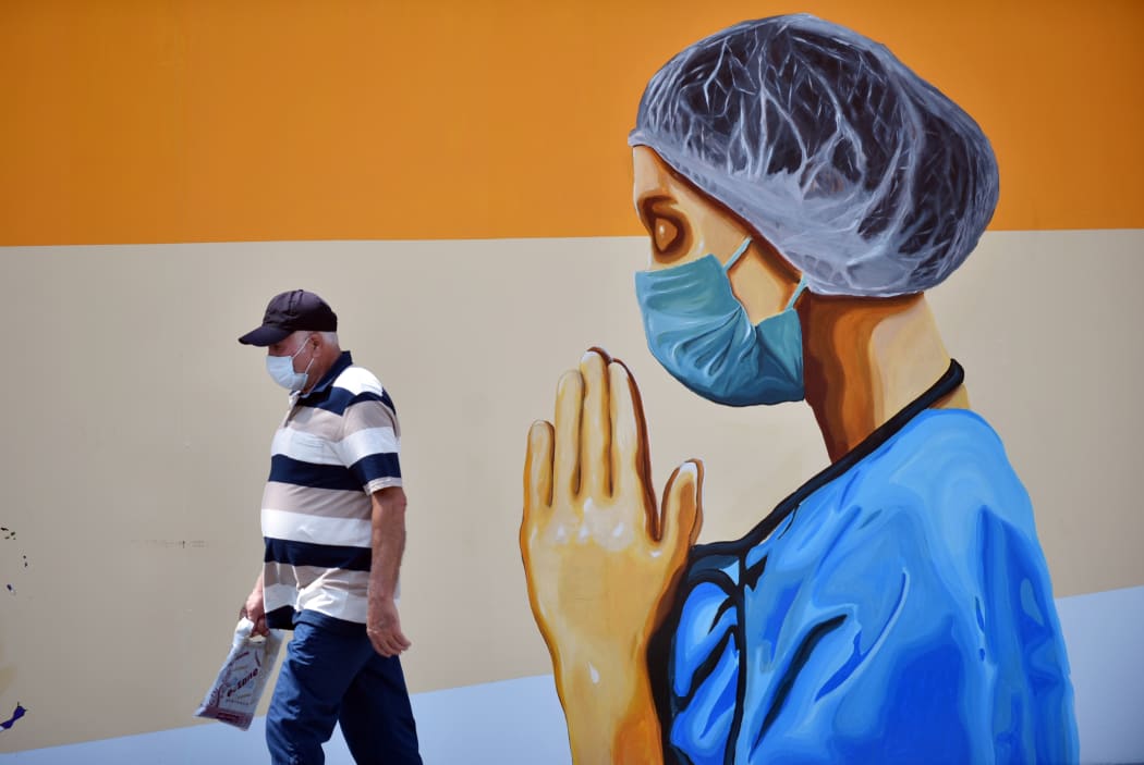 A man wearing face mask walks past a mural depicting of a healthcare worker and a world map with flags on walls of idle cinema building in Mersin, Turkey on June 23, 2020.