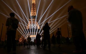 Attendees take pictures of the Eiffel Tower as lasers light up the sky during the opening ceremony of the Paris 2024 Olympic Games in Paris on July 26, 2024. (Photo by Martin  BERNETTI / AFP)