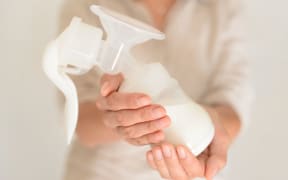 Mother holds breast pump in her hand, blurred background