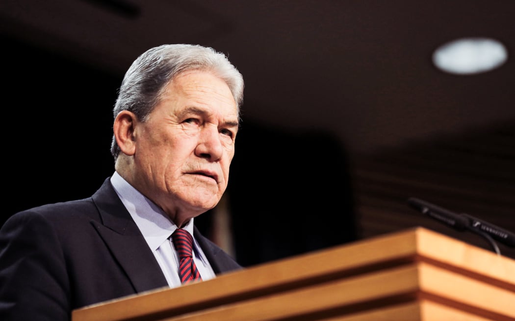 Winston Peters standing in the Beehive Theatre, making an announcement.