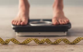 Person standing on weigh scales, tape measure in the foreground.