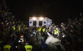 Rescuers and spectators look on as an ambulance drives away from the rescue scene.