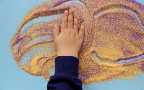 Baby hands plays with colorful sand. Child fine motor skills development. Creative kids occupation. View from above