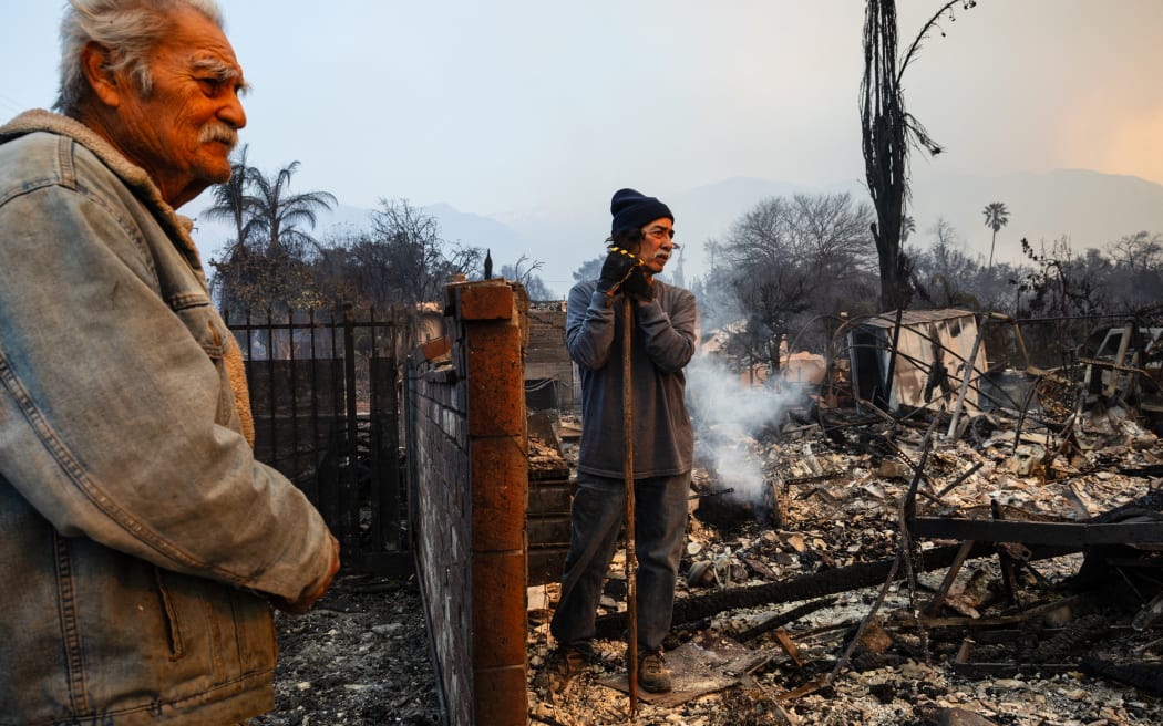 Richard Castaneda (L) and Rupert Garcia look at the ruins of Garcia's home destroyed by the Eaton Fire in Altadena, California, on January 9, 2025. Both Garcia and Castañeda lost their homes in the Eaton Fire. Wildfires threatened to engulf parts of Hollywood on January 9 as a growing number of blazes raged across Los Angeles, forcing over 100,000 people to flee their homes and claiming at least five lives. (Photo by Zoë Meyers / AFP)