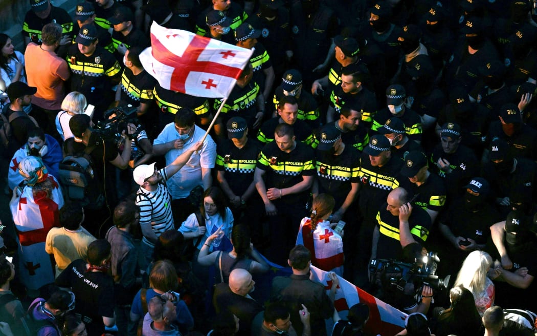 Demonstrators face police officers and hold a Georgia's flag outside the Georgian parliament during a rally against a controversial "foreign influence" bill, which Brussels warns would undermine Georgia's European aspirations, in Tbilisi on May 1, 2024. (Photo by Vano SHLAMOV / AFP)