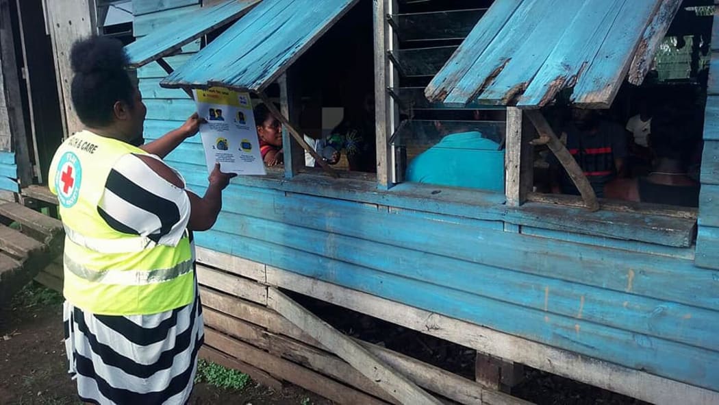 A Red Cross volunteer shares a message about Covid-19 transmissions through a window to a family in Uciwai Settlement, Nadi.