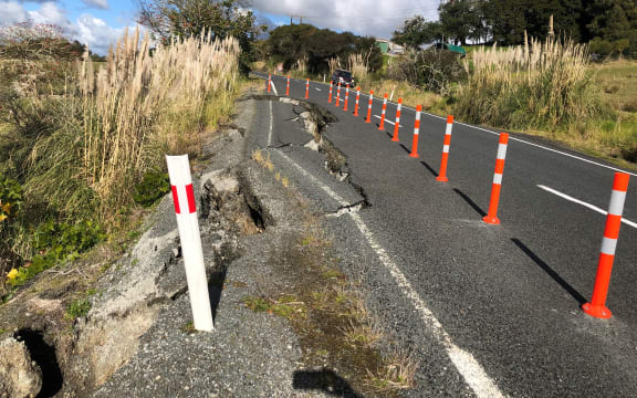 A slump on the side of a two lane road. It has been closed off with orange marker poles.