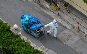 A worker in Shanghai wears PPE, and pulls along a cart filled with trash.