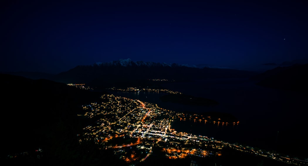 Beautiful night view of Queenstown with the snow capped mountains in the background taken during an orange sunset from the Queenstown, New Zealand Skyline