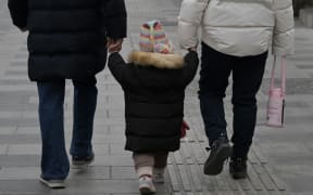 A toddler walks with two adults on a street in Beijing on January 17, 2024. China's population decline accelerated in 2023, official data showed on january 17, 2024, extending a downward streak after more than six decades of growth as the country battles a looming demographic crisis. (Photo by Pedro PARDO / AFP)