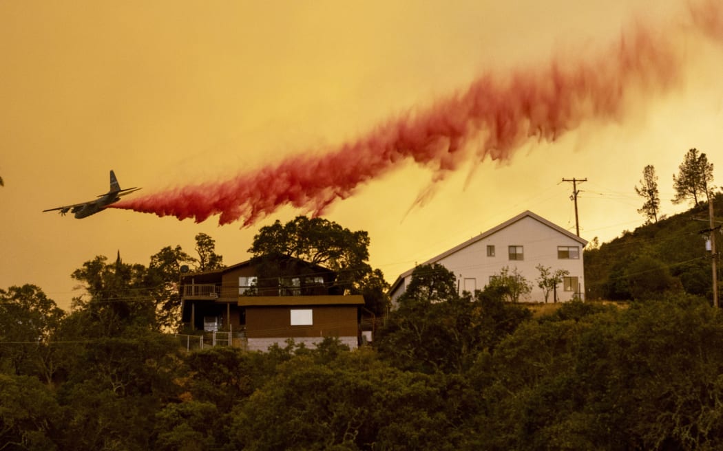 An airplane drops fire retardant over homes in the Spanish Flat area of Napa, California as flames rage through on August 18, 2020.